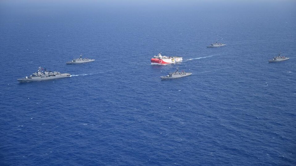 Un navire est escorté par plusieurs bateaux militaires.