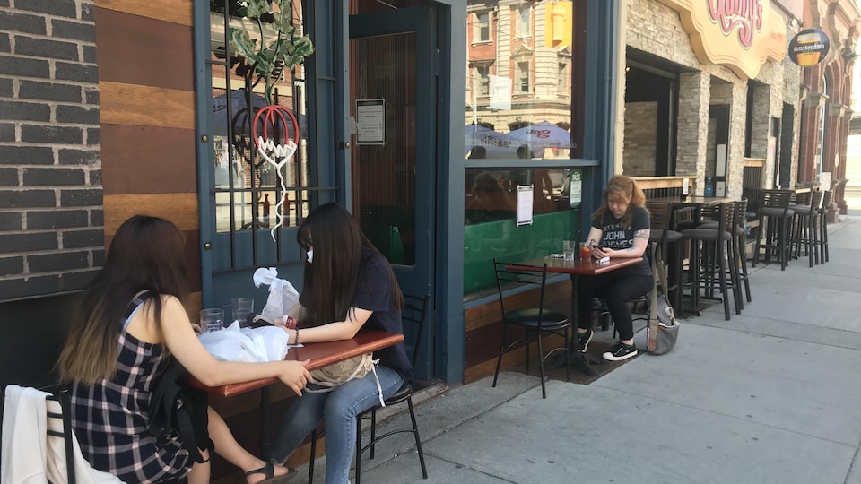 Des clients assis à des tables extérieures, sur le trottoir, devant un restaurant.