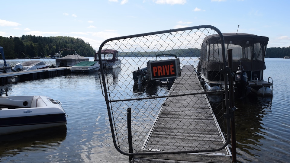 Un quai dont l'accès est barré par une clôture sur laquelle est affichée une pancarte indiquant « Privé »; en arrière-plan un ponton et un bateau à moteur amarrés au quai