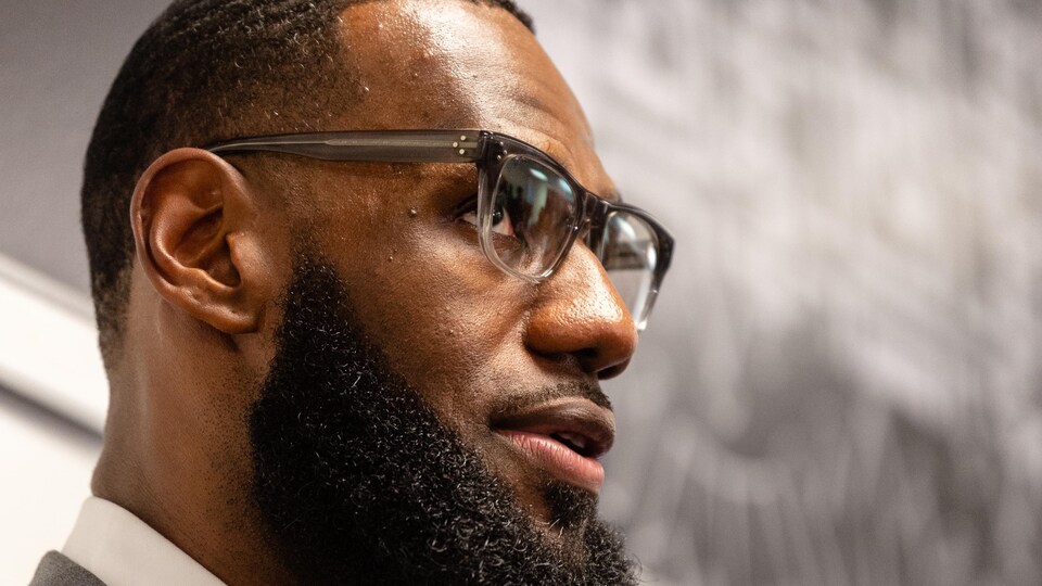 Un homme noir portant des lunettes et une barbe bien taillée est photographié de profil alors qu'il lève les yeux vers le haut.