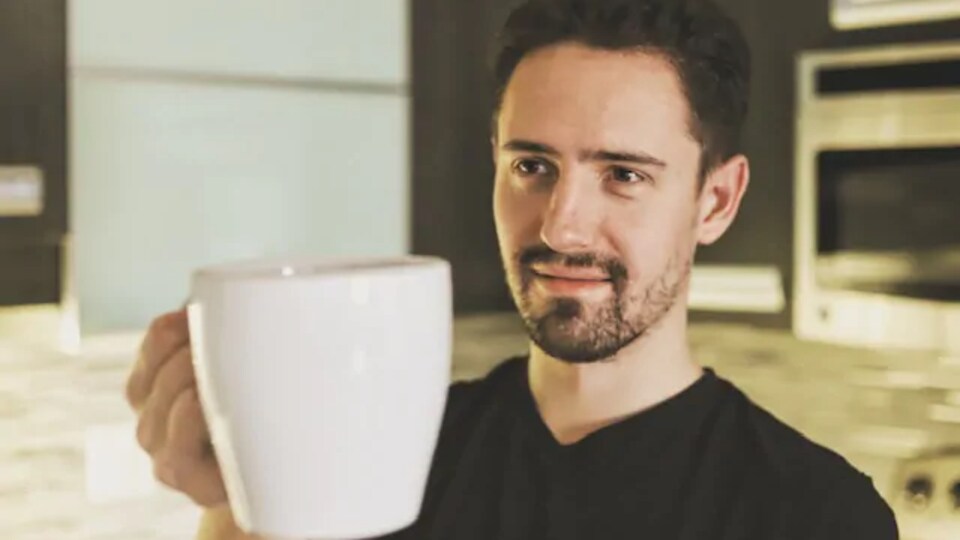 Un jeune homme tient une tasse de café dans ses mains.