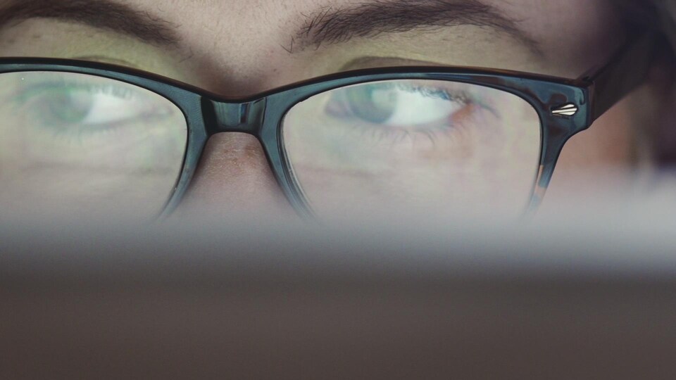Une personne portant des lunettes regarde un écran.