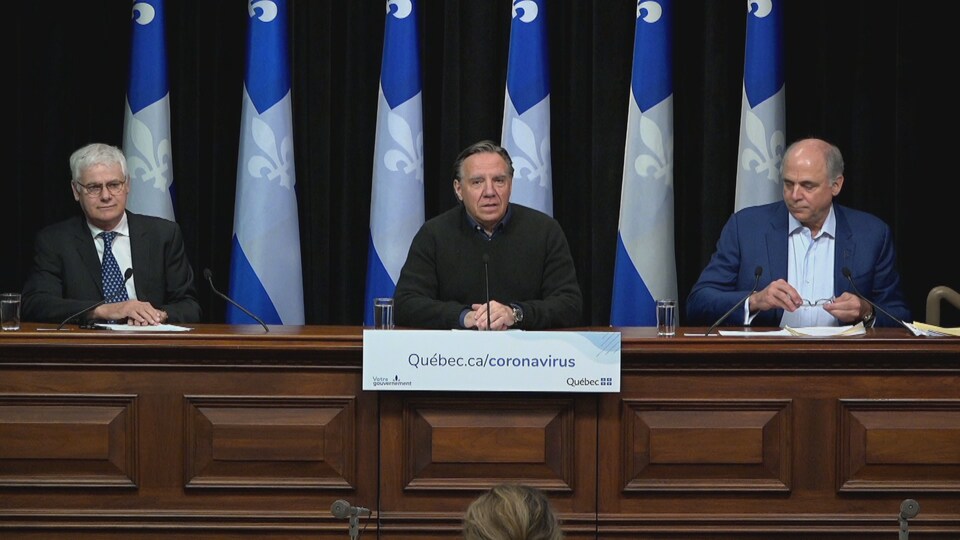 Le Dr Richard Massé, François Legault et Pierre Fitzgibbon en conférence de presse devant des drapeaux du Québec.