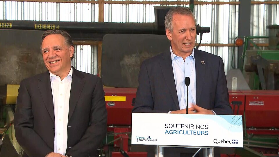 Le ministre André Lamontagne prend la parole, aux côtés du premier ministre François Legault, avec en arrière-plan de l'équipement agricole.