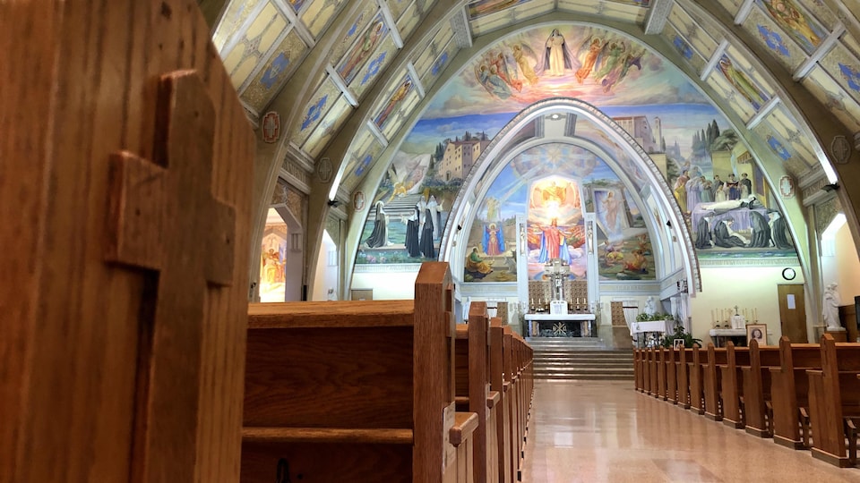 L'intérieur d'une église. On voit des bancs et des fresques au plafond.