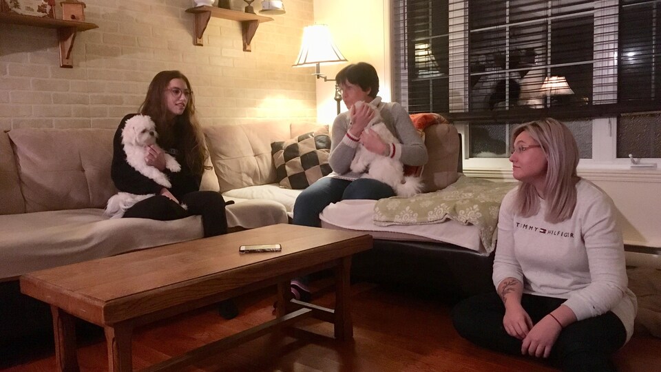 Trois femmes sont assises sur le divan dans un salon. Deux chiens sont aussi sur la photo.