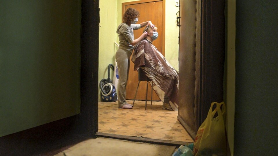 Une femme, Lena, coiffe une cliente dans sa maison. 
