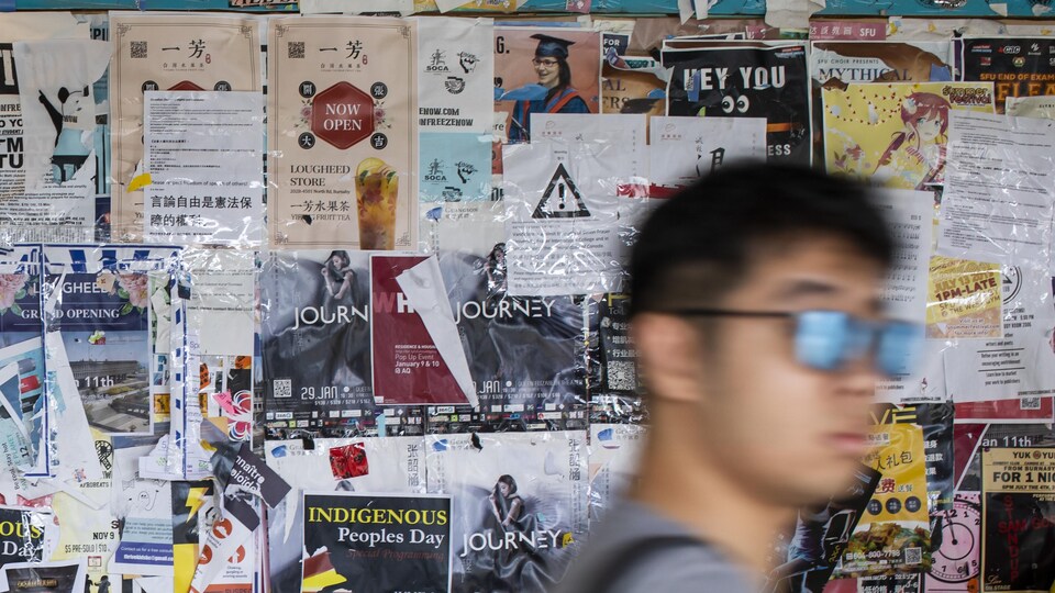 Un étudiant passe devant un mur d'affiches diverses. 