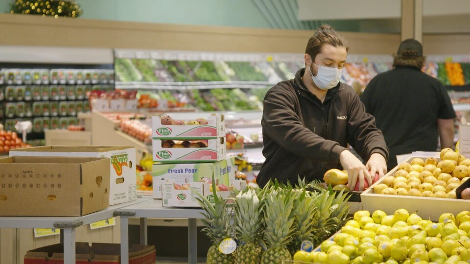 Un homme place des fruits dans les étals d'une épicerie.