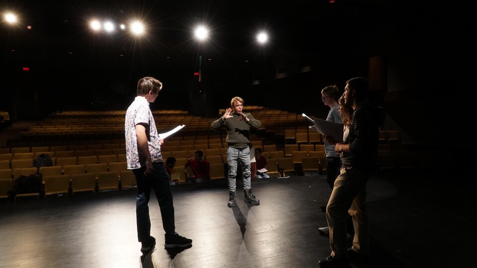 Un homme sur scène donne des instructions à quatre acteurs qui l'écoutent attentivement.