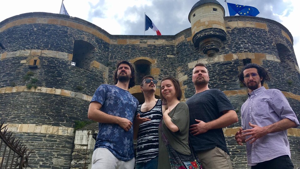 Quatre hommes et une femme en contreplongée devant un château français.