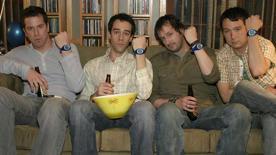 Les quatre hommes sont assis sur un divan et montrent leur montre.