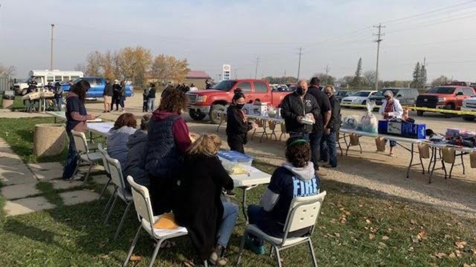 Des gens sont assis à une table placée dehors. À l’arrière, il est possible de voir des prix.