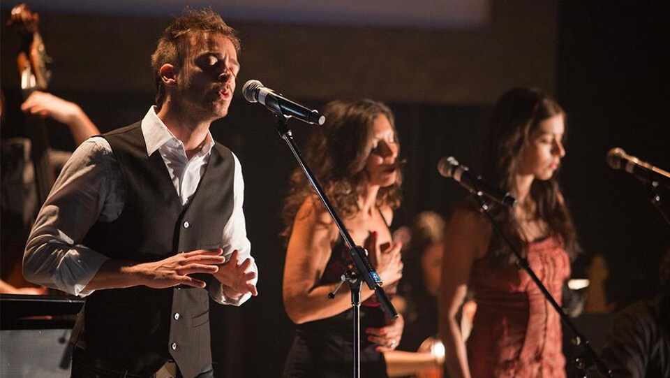 Trois artistes chantent devant un micro.