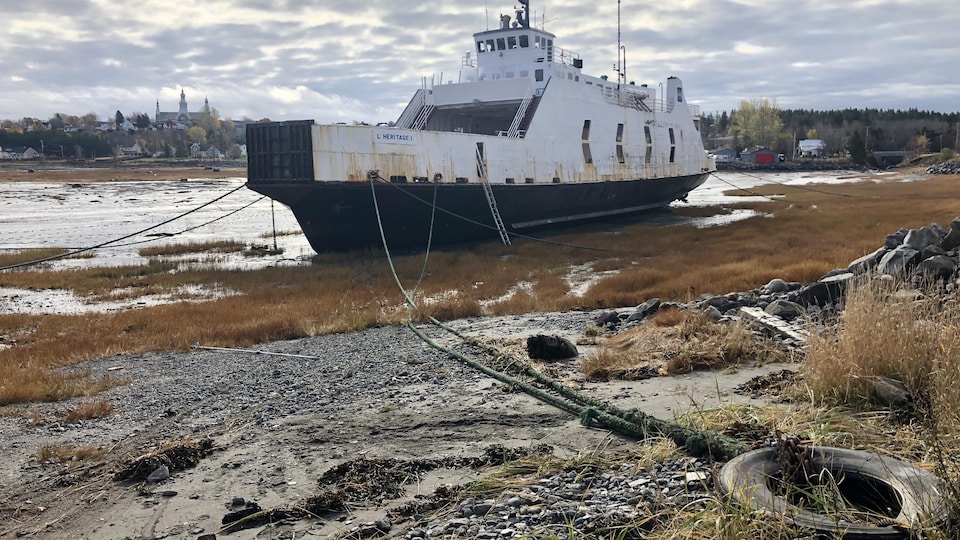 Le navire amarré dans une baie, à marrée basse. En arrière-plan, la ville de Trois-Pistoles.