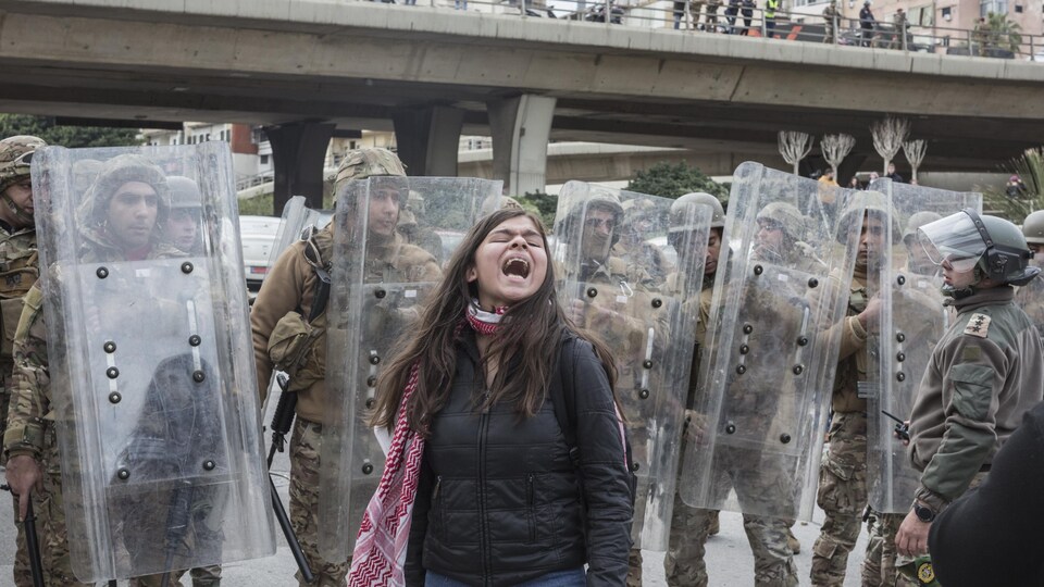 Une femme crie devant une rangée de militaires casqués, armés de matraques et protégés par des boucliers. 