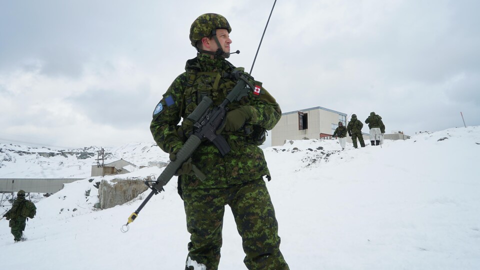 Un militaire avec son fusil mitraillette se tient debout dans la neige en regardant à gauche.