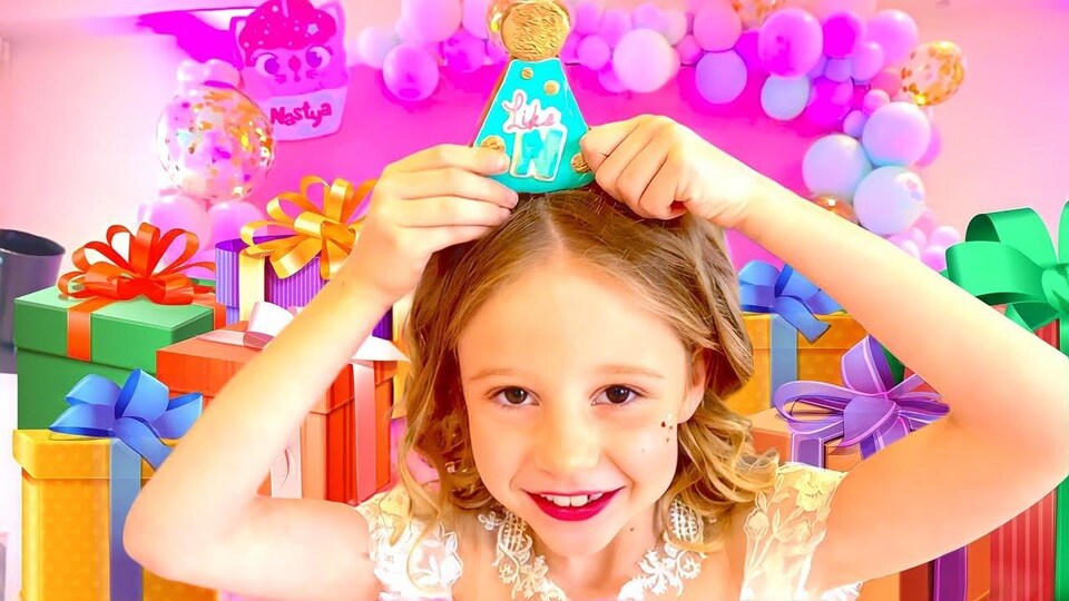 Une fillette enfile un biscuit en forme de chapeau de fête sur sa tête, devant un décor très coloré.