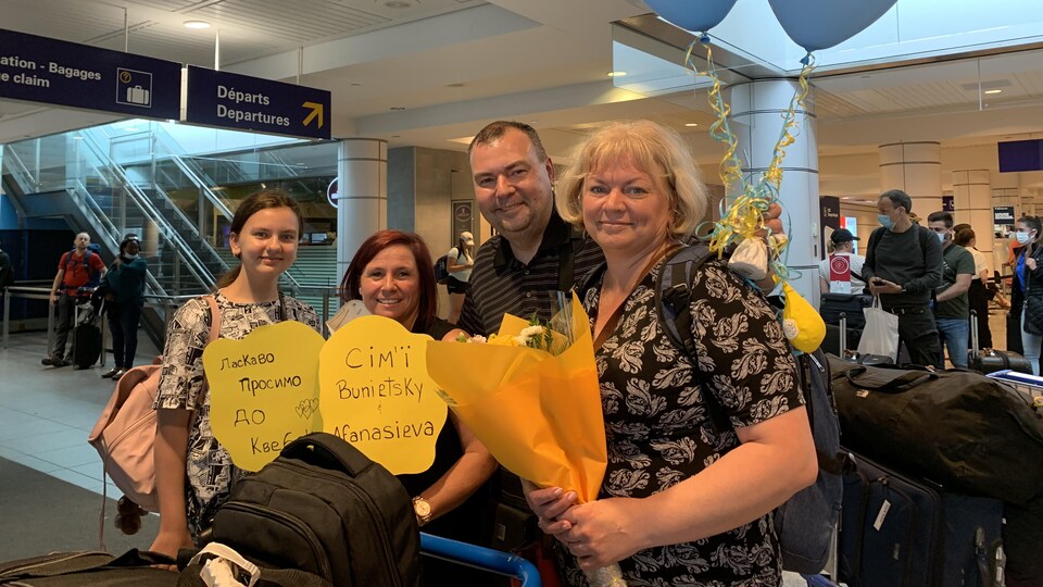 Trois femmes et un homme avec des ballons et des fleurs à l'aéroport.