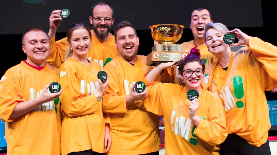 Un groupe de personnes vêtues de chandails jaunes soulèvent un trophée.
