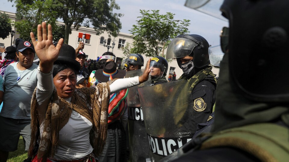 Une femme lève les bras devant des policiers antiémeutes.