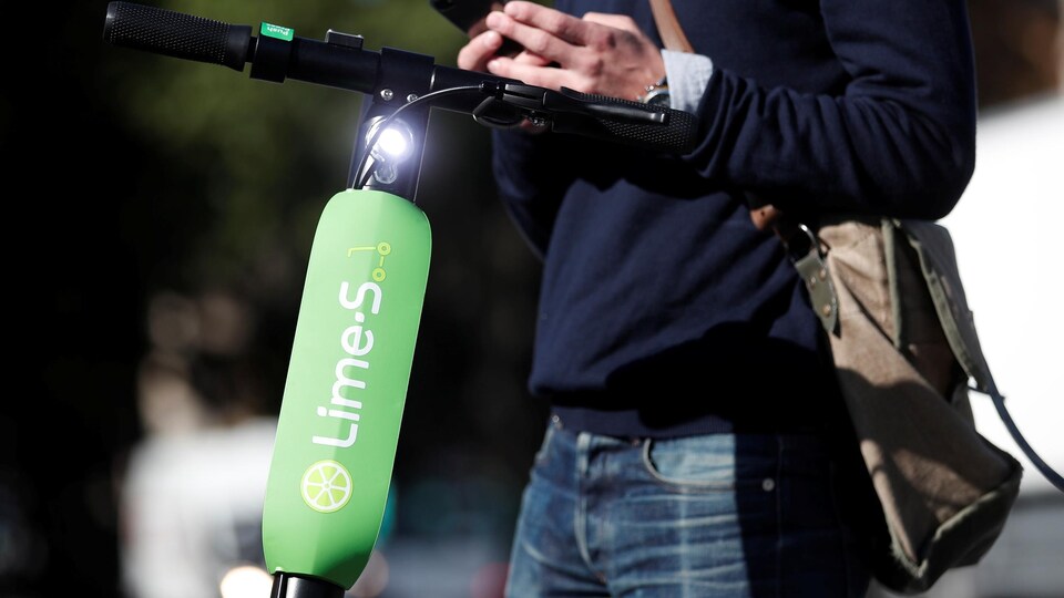 Un homme regarde son cellulaire près d'une trottinette électrique de marque Lime.