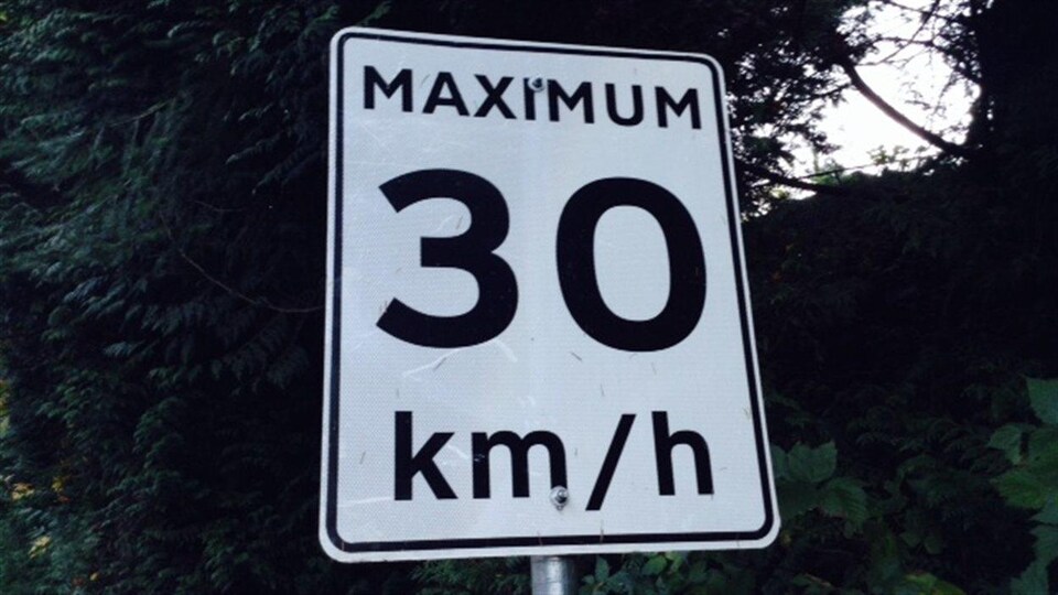 Gros plan d'un panneau blanc limitant la vitesse à 30 km/h.