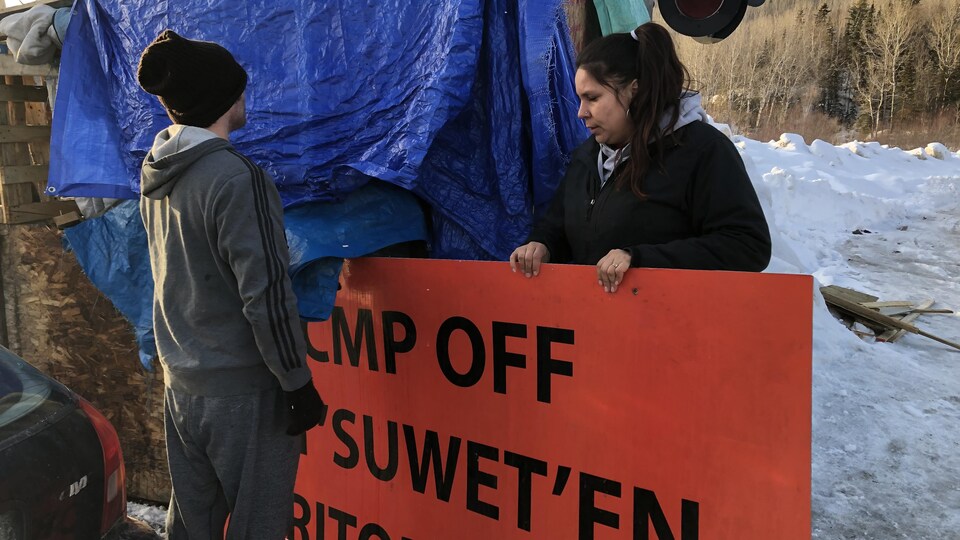 Des gens qui enlèvent une affiche installée sur le campement des Micmacs de Listuguj.