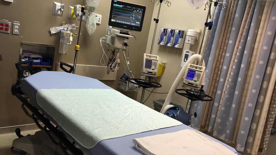Un lit d'hôpital vide avec des machines et de l'équipement de soins médicaux ainsi qu'un moniteur.