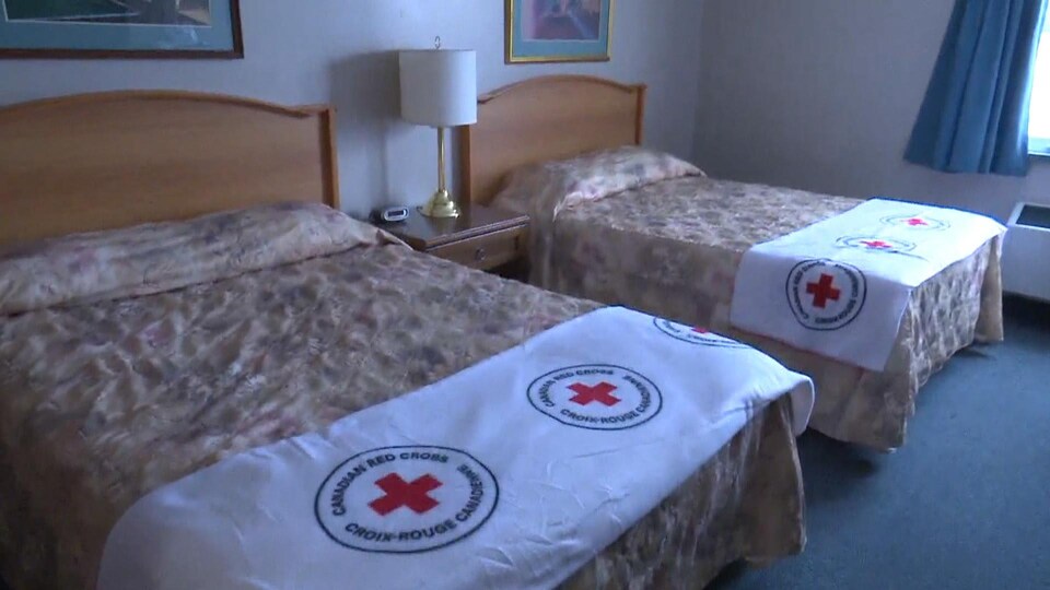Une chambre d'hôtel équipée de deux grands lits et de draps frappés du logo de la Croix-Rouge.