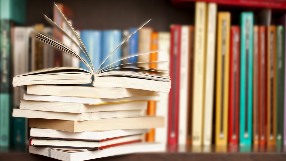 Pile de livres sur une étagère avec un livre ouvert et des livres rangés en arrière-plan.