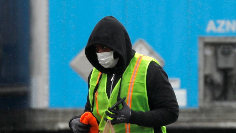 Un livreur de marchandise portant un masque de protection devant trois gros camions.