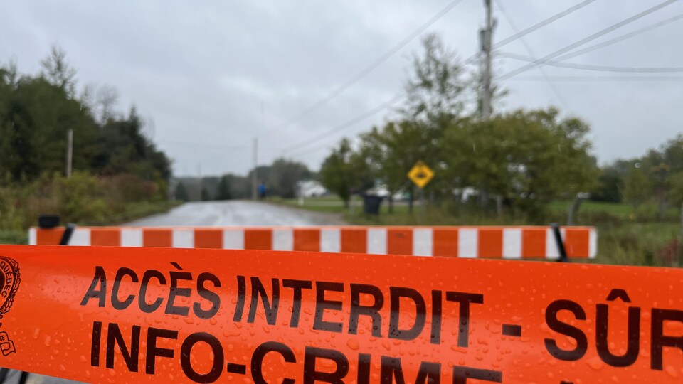 Un ruban orange de la Sûreté du Québec bloque une portion du rang sur lequel s'est produit l'accident à Locher. Sur le ruban, on peut y lire « accès interdit » et « Info-Crime ».