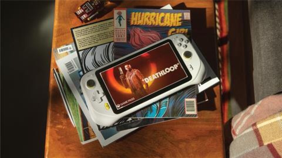Un appareil ressemblant à une console de jeux vidéo affiche le titre «Deathloop», au dessus d'une pile de boîtiers de jeux vidéo sur une table de salon. 