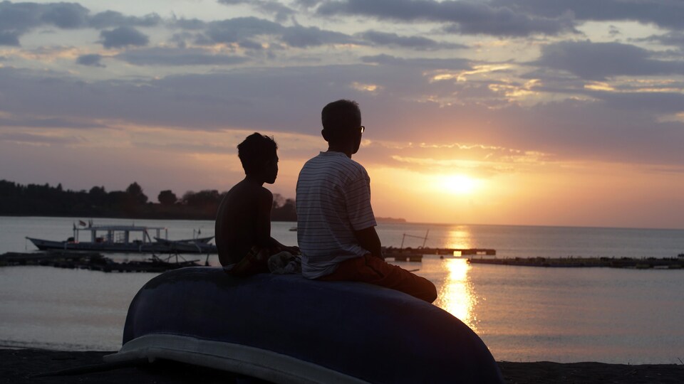 Deux hommes assis face à la mer observent un coucher de soleil. 