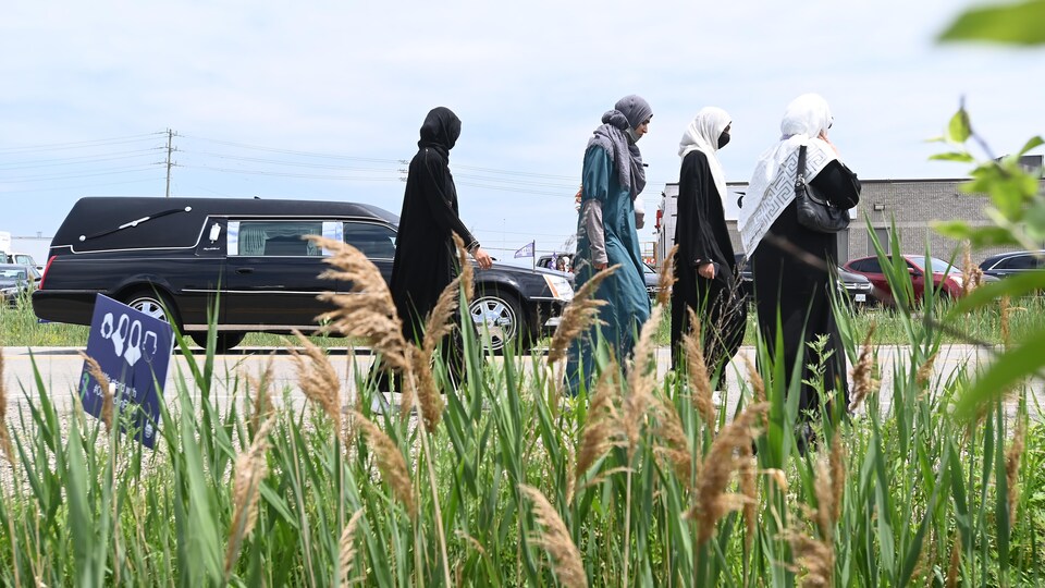 Quatre femmes voilées marchent à côté d'un corbillard.