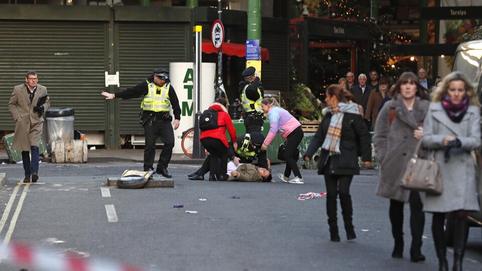 Des policiers et des passants se pressent autour d'une personne allongée au sol. 
