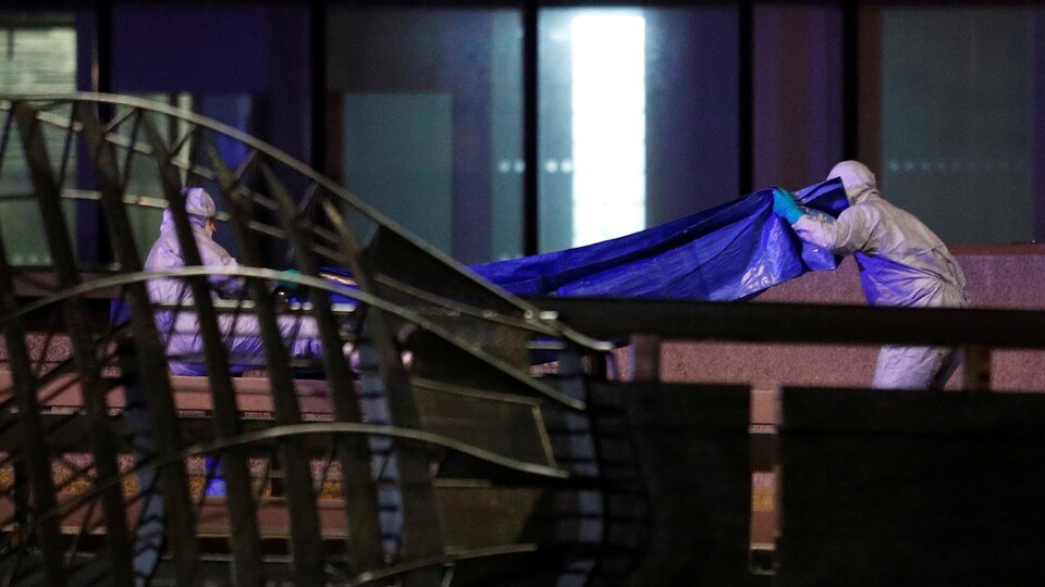 Deux travailleurs en combinaison manipulent une bâche sur un pont.