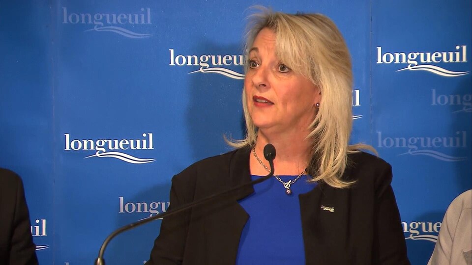 La mairesse de Longueuil Sylvie Parent devant un panneau sur lequel figure le logo de la Ville.