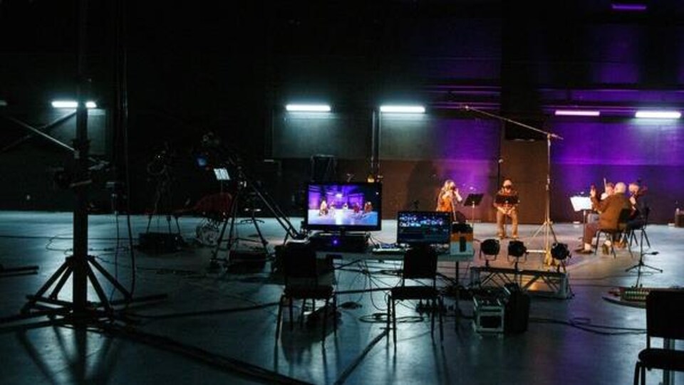 Dans un immense studio d'enregistrement vidéo sombre, les musiciens sont sous un éclairage coloré.