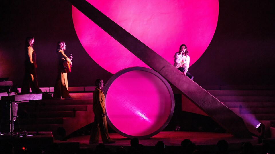 Singer Lorde sings on a stage as musicians walk towards him.