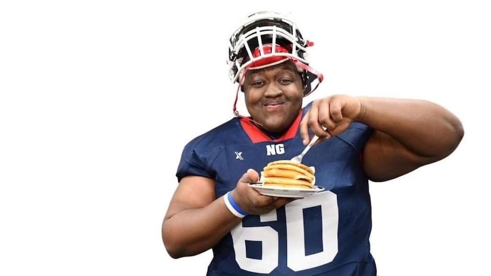 Loris Tyson Ndongozi, dans son uniforme de football, tenant dans ses mains une fourchette et une assiette remplie de grosses crêpes.