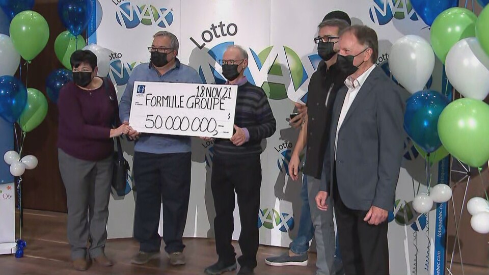 Des adultes tiennent un chèque géant indiquant 50 millions de dollars devant un paravent de Lotto Max