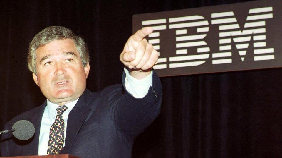 On voit M. Gerstner devant un micro, qui parle en pointant son doigt devant lui, le regard levé. Derrière lui, le logo des trois lettres d'IBM.