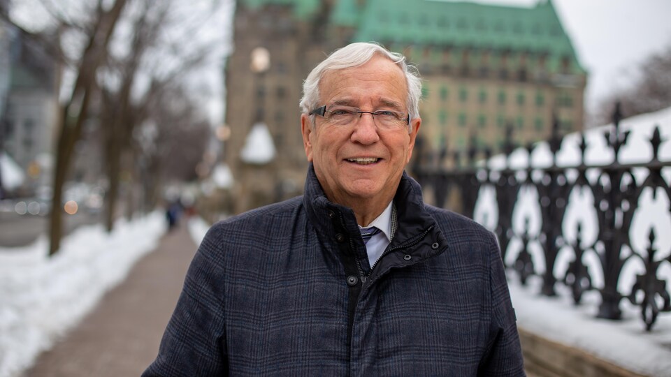 Louis Plamondon qui sourit en regardant la caméra pendant qu'il marche dans la rue, l'hiver.