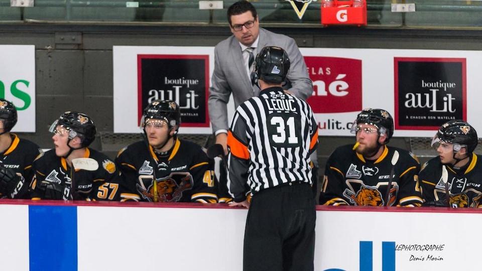 Un homme en complet sur le banc des joueurs pendant une partie de hockey.