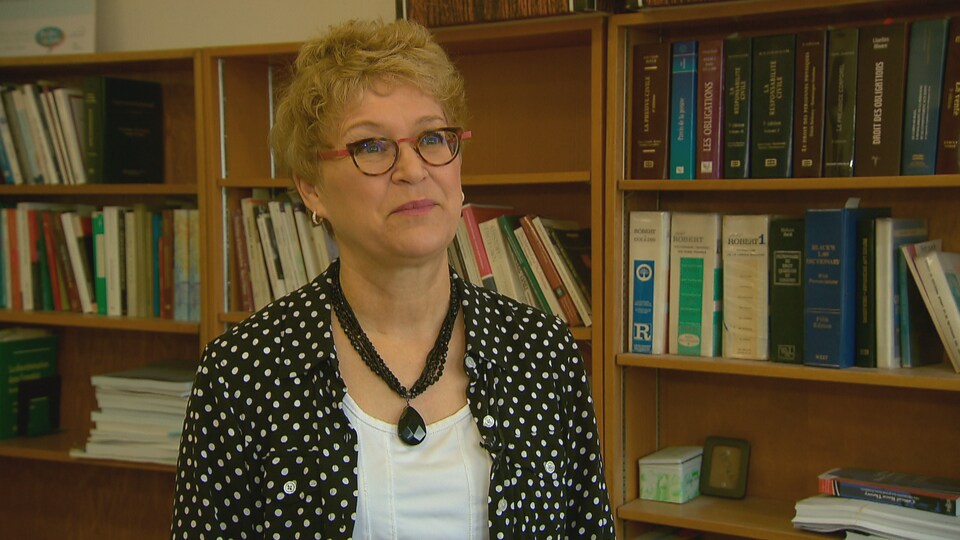 Louise Langevin accorde une entrevue à Radio-Canada dans son bureau situé à l’Université Laval. On aperçoit, à l’arrière-plan, des ouvrages de référence rangés dans des étagères.