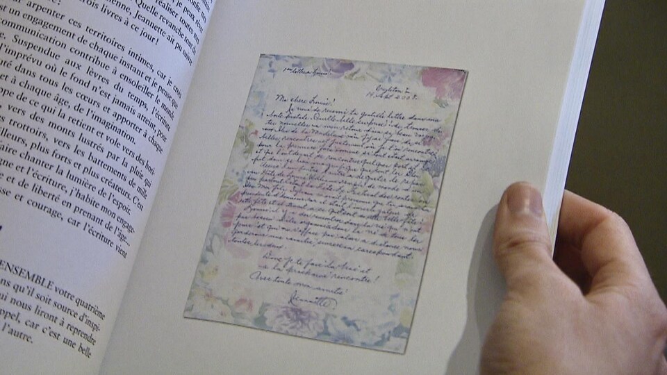 Une main tient le livre, où la page montre un exemple de lettre.
