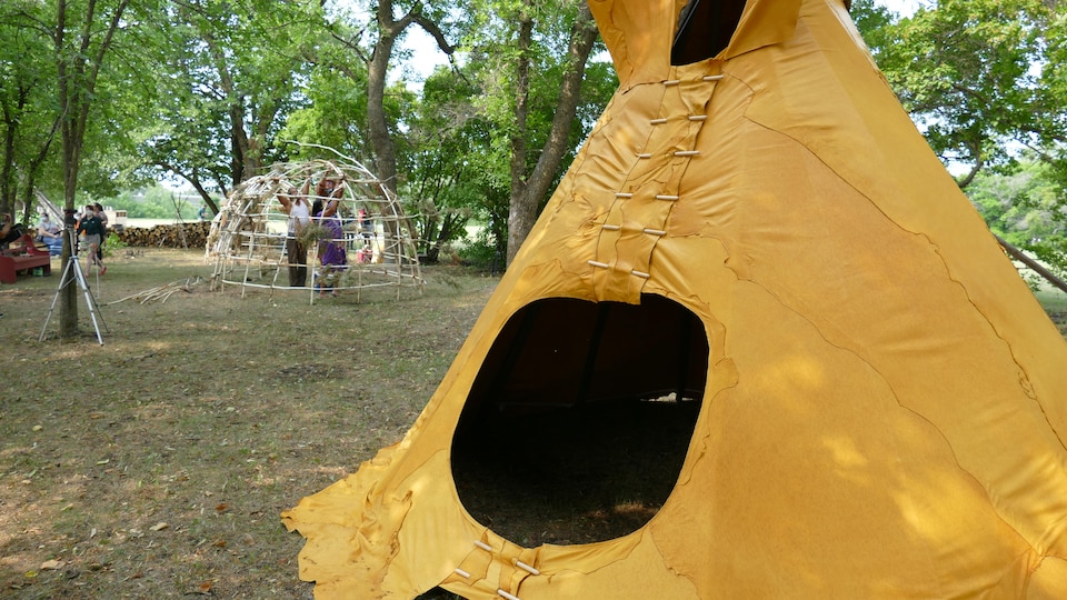 À l'avant-plan, le tipi orange et derrière, le wigwam en construction.
