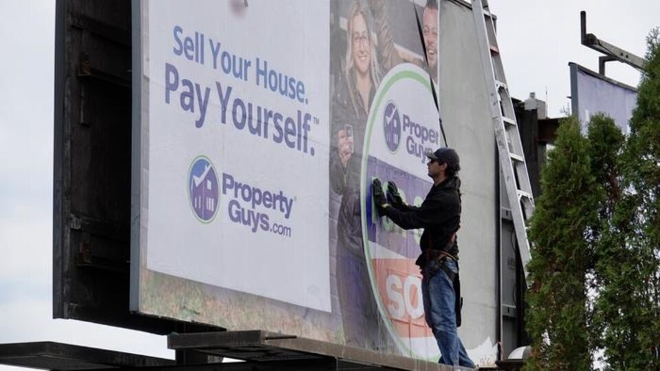 Un travailleur installe une publicité de propertyguys.com sur un grand panneau